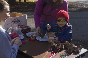 Peanut Butter Pinecone Birdfeeder craft station with young boy and mother