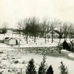 Historic Kellogg Bird Sanctuary Buildings in the winter with snow on the ground and frozen lake. Swans, ducks, and geese can be seen standing on the ice.