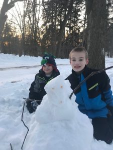 Image of 2 boys in snow suits with a snowman