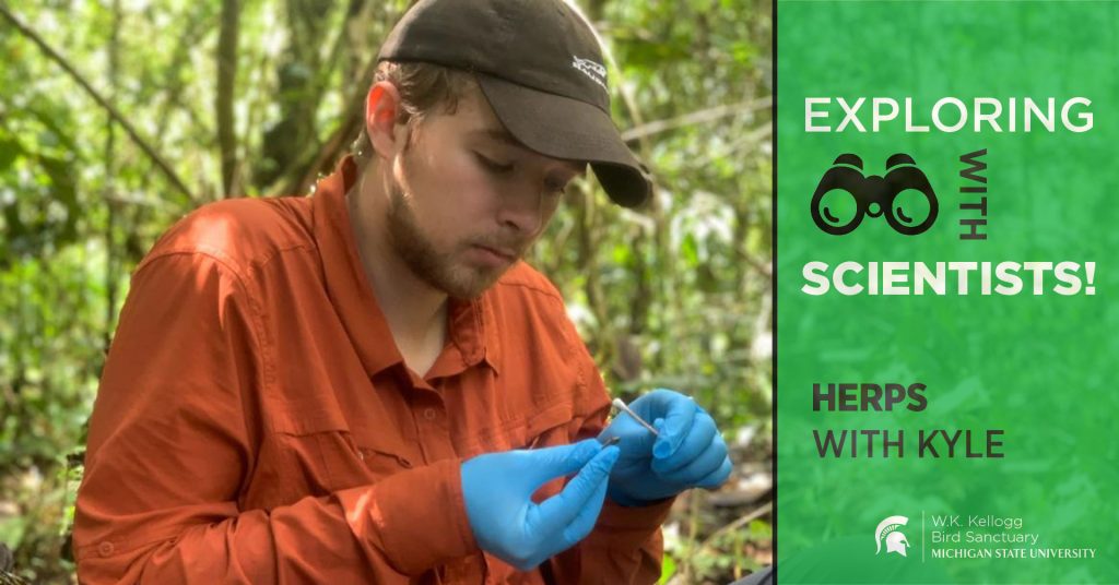 Kyle Jaynes sits in a forested area, looking down at a small object in his hands. Text overlay reads Exploring with Scientists! Herps with Kyle.