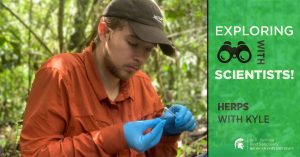 Kyle Jaynes sits in a forested area, looking down at a small object in his hands. Text overlay reads Exploring with Scientists! Herps with Kyle.