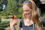 Woman holding orange and black monarch butterfly in her hand in a garden.