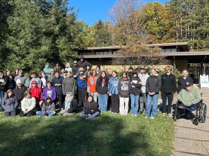 Image of a group of students in front of a brown building, standing on grass