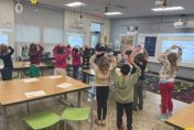 Image of a classroom with students with hands over heads forming a mushroom cap