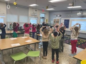 Image of a classroom with students with hands over heads forming a mushroom cap