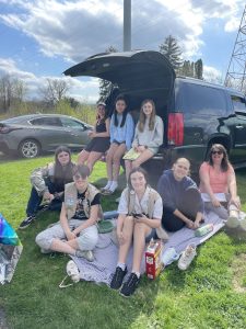 Image of girl scouts sitting on the ground and the tailgate of a van in the sunshine